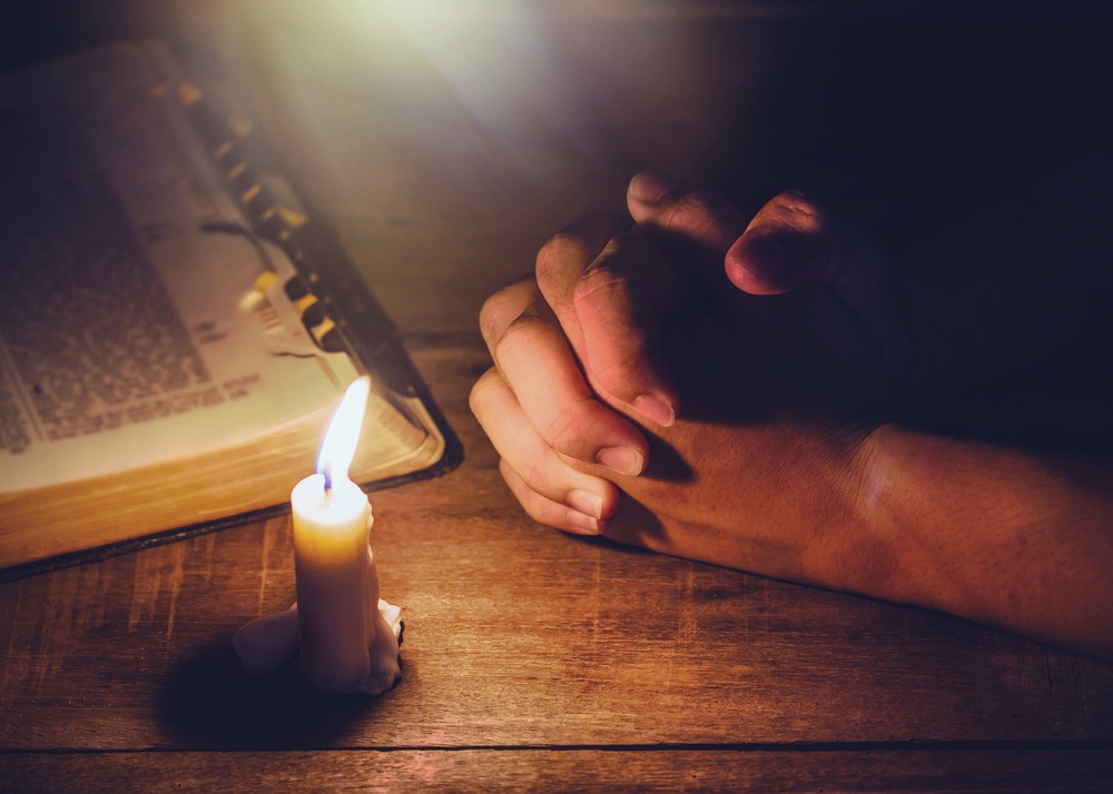 Image representing hands in prayer and candle