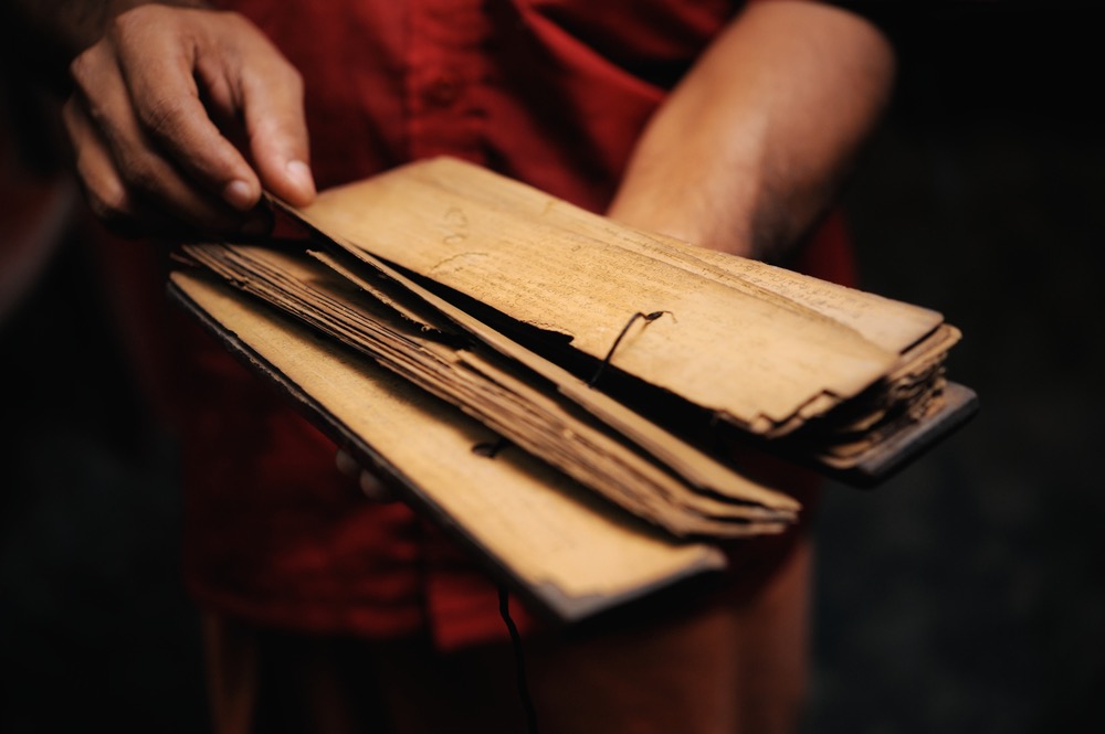 Monk holding ancient Sanskrit manuscript representing Vedic meditation lineage and traditional teachings