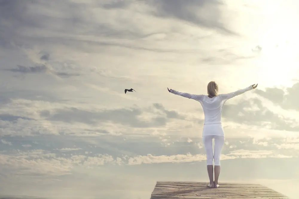 Woman standing tall in front of a sunrise experiencing joy